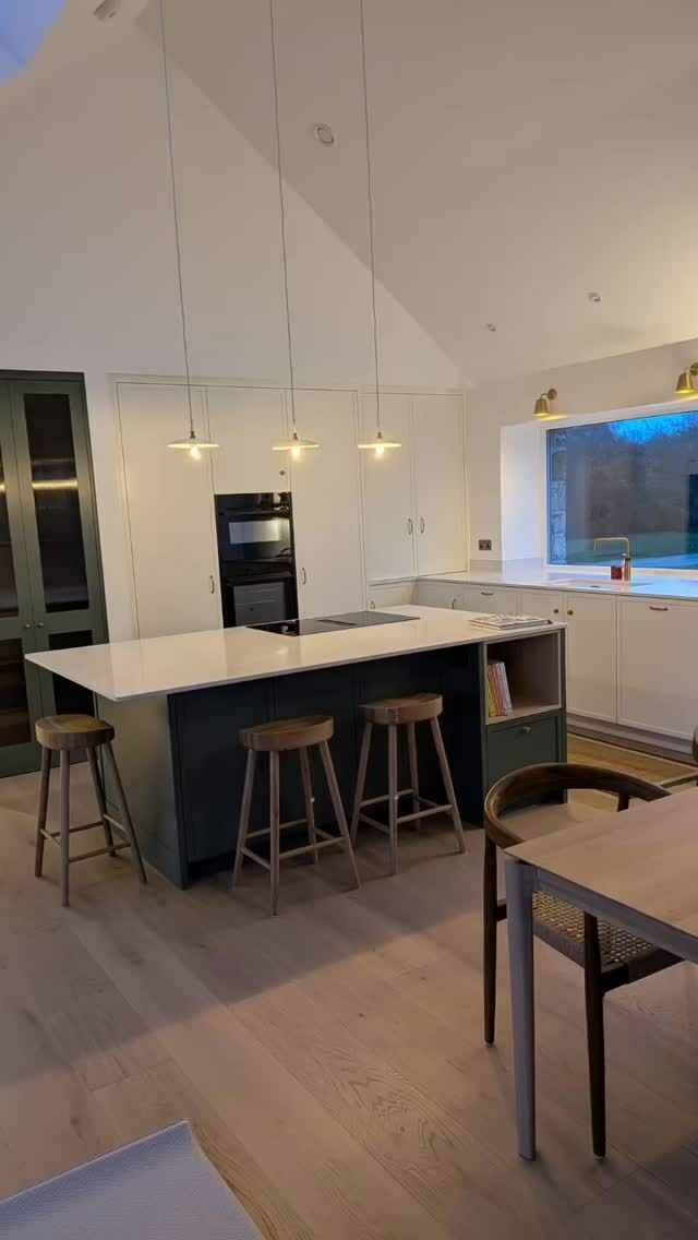 This kitchen has a bright, contemporary feel with warm, refined details.  The open plan kitchen centered around a large island with Neff vented hob and space for stools making the island both prep space and social hub.  The glass doors are into hidden pantry area.  The lights give the room a lovely ambient feeling and the high vaulted ceiling enhances the sense of space.  This kitchen blends modern minimalism with classic touches, feeling elegant yet practical.  All Neff appliances plus Silestone Calacatta gold quartz worktop. #modernkitchen #bespokekitchen #worktop